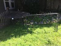 Photo showing the round wrought iron table top leaning against a fence outdoors with grass and rocks in the background.