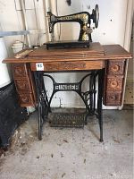Full front view of vintage Singer sewing machine on cast iron treadle base and oak cabinet with carved drawer fronts.