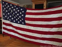 Front side view of one large American flag with 50 stars and 13 stripes hung indoors for display.