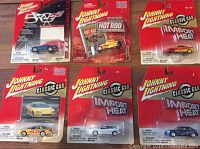 Front view of six Johnny Lightning die cast cars in original packaging from 2003. Various models including Corvette, Hot Rod, and Classic Car Import Heat series.
