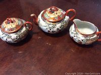 Photo showing three Kutani ware pieces including teapot, sugar bowl, and creamer on wooden surface