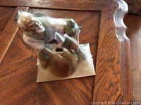 Porcelain figurine of Chinese man in traditional attire, seated and working, viewed at an angle on wooden surface.