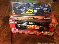 Two Racing Champions NASCAR die-cast cars in unopened boxes with clear display windows, stacked one above the other, shown on wooden floor.