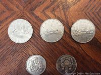 Three Canadian silver dollar coins (1980, 1980, 1981) and two fifty cent coins (1969, 1971) on wooden surface.