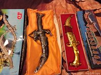 Two decorative knives displayed in their boxes, one with a silver dragon design and the other with a gold-tone design