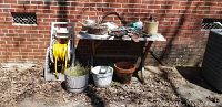 Photo showing the weathered wood table with various garden items placed on top and underneath, including pots and a jug, plus hose reel on the left side.