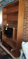 Full view of the tall wooden shelf unit with five shelves and a central cutout area for TV.