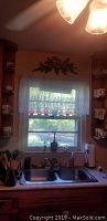 Photo of kitchen window above sink showing multiple colored crackled glass pitchers lined on the windowsill.