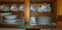 Kitchen wooden cabinet with stacked Pier 1 Sable pattern plates, bowls, and hanging mugs in floral blue and red design.