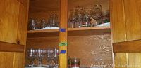 Open wooden cabinet shelves with various sizes of Christmas-themed glasses including stemware and tumblers, some with holly and red ribbon designs