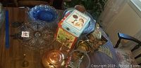 Overview photo showing glass plates, copper kettle, brass items, tins on wooden table