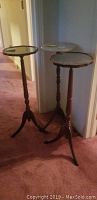 Photo showing three tripod plant stands, two with dark wooden round tops and one with a white marble round top.