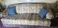Front and side angle views of the heavy sofa showing floral upholstery, wood framing on armrests, and included blue throw pillows.