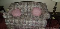 Full front view of floral upholstered love seat with two pink round throw pillows and lumbar pillow