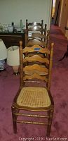 Photo showing four wooden ladder back dining chairs with caned seats in a row, placed indoors on a carpeted floor.