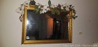 Frontal view of the beveled mirror with gold-colored wooden frame and faux flower garland draped over the top edge.