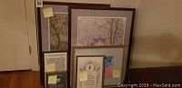 Photo showing a group of framed art pieces piled on floor, showing variety of sizes and themes.