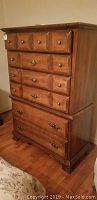 Front view of wooden chest of drawers showing brass hardware and drawer arrangement.