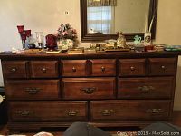 Full front view of the wooden dresser showing nine drawers and brass-colored hardware knobs and handles. Items on top not included.