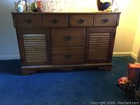 Front view of a medium brown wooden buffet showing three drawers on top, two shuttered cabinet doors with black metal handles below, standing on a blue carpet.