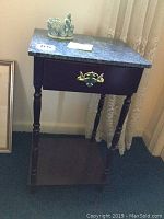 Wooden end table with marble top in corner, showing single drawer with brass handle and turned legs.