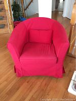 Front view of red slipcovered IKEA upholstered chair with matching pillow on hardwood floor.