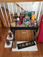Table with assorted candles of different shapes, colors, and sizes including pillar, votive, and spherical candles along with some candle holders on a black glass table.