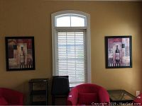 Two black-framed Gregory Gorham prints hanging on a yellow wall beside a window, showing wine bottle and wine glass designs.