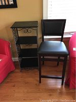 Full view of black wooden shelving unit with ornate metal sides and the dark wood folding chair with padded seat and backrest.