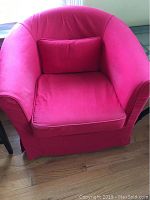 Front view of the red slipcovered chair with matching pillow, showing curved armrests and cushioned seat covered in red fabric