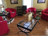 Full view of living room corner showing red chairs and three metal framed glass tables: one coffee table and two end tables.