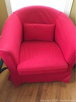 Front view of IKEA upholstered chair covered with red slipcover and matching pillow on seat.