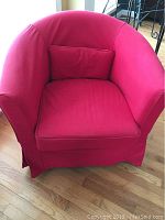 Front view of the IKEA upholstered chair with red slipcover and pillow on hardwood floor.