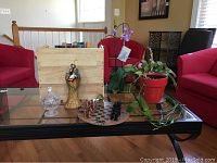Glass coffee table with the chess set, several potted plants, cut glass candy dish, Holy Family figurine, and wooden wine rack arranged on top.