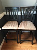 Full view of two matching wooden dining chairs with padded beige seats.