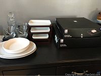 Lot on dark surface showing the decanter, martini glasses, white ceramic serving plates and bowl, tiered appetizer stand dishes, Umbra boxes for chip and dip and Lazy Susan, and white ceramic dishes on wood stand.