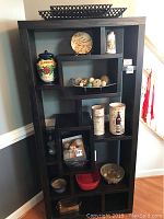 Front view of dark wooden shelving unit with decorative jars, plate, woven balls, and other small items on multiple shelves.