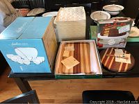 Overview of punch bowl box, two hardwood cutting boards with packaging, rotating cake stand, and cheese spreader on table
