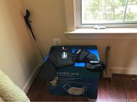 Wide shot showing Breg Freestyle OA knee brace, Mueller back brace, and Carex raised toilet seat box leaning against wall with mobility aids.