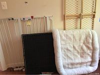 Unassembled large black metal dog crate frame, white metal dog gate, and beige and white plush dog bed