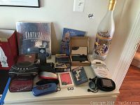Photo showing the full lot including Disney Fantasia 2000 DVD in wrapper, Garmin Nuvi 30 GPS, Sharper Image clock radio, mini vacuum, sunglass cases, earbuds, charger wallet, bedding and Van Gogh vodka bottle.