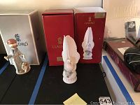 White dove figurine with wings raised, positioned in front of the original red Lladro box and another white Lladro box, showcasing the figurine and its packaging.