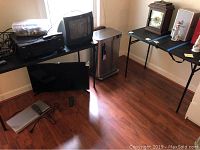 Wide view showing the two folding tables with various items on top and the Simplehuman waste bin between them on the floor.