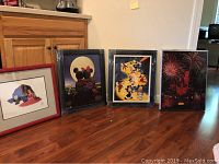 Four framed Disney-themed art pieces arranged on floor next to kitchen cabinet, showing the full set in original packaging wrap