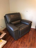 Front right angled view of black leather electric recliner chair positioned near wall on wooden floor. Shows padded armrest, seat, backrest, and side controls for reclining.