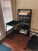 Wide shot showing TV table next to bookshelf with a laminator and other items on shelves, black cabinet partially visible.