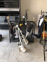 Photo showing child's golf clubs, rolling golf caddy with white wheels, and black metal rack in background