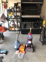 Full view of blue clothes steamer with telescopic handle, Bissell Revolution floor steam cleaner, Swiffer Carpet Flick with two boxes of refills, a dustpan and brush.