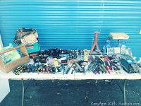 Full view of the large collection of various hand tools, pliers, screwdrivers, a Makita tool bag, jack stand, and other tools laid out on a table.