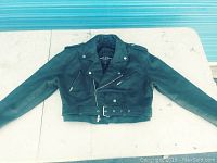 Full view of black leather motorcycle jacket laid flat with arms extended, showing design and condition.